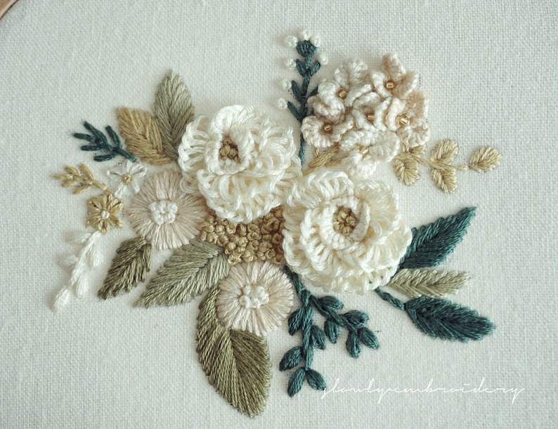 May include: Hand-stitched floral embroidery featuring cream-colored flowers, accented with green, beige, and gold thread. The detailed needlework showcases a variety of stitches, creating a textured, three-dimensional effect. The artwork is set against a white linen background.