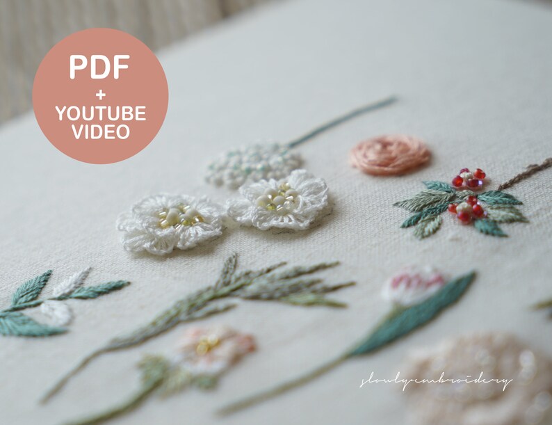 以下が含まれることがあります： 様々な手刺繍の花柄が施された白い布のクローズアップ。真珠のような中心を持つ白い花、ピンクとピーチ色の花、緑の葉が含まれています。画像には「PDF + YOUTUBE VIDEO」というテキストも含まれています。