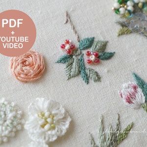 以下が含まれることがあります： クリーム色の生地に刺繍された花のクローズアップ。バラ、チューリップ、その他の詳細な花柄など、さまざまな花が写っています。「PDF + YOUTUBE VIDEO」というテキストがピンク色の円の中にあります。