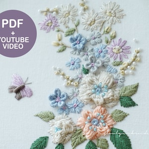 May include: Hand-embroidered floral design featuring a variety of flowers in pastel colors, including light blue, peach, and lavender, with green leaves and a butterfly. The design is on a white fabric, with the text "PDF + YOUTUBE VIDEO" in a purple circle.