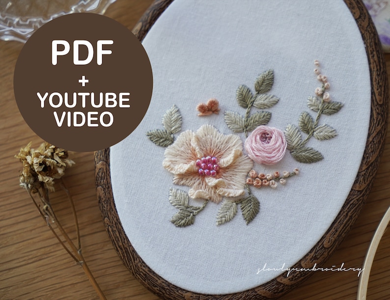 Puede incluir: Bastidor de bordado ovalado con dise&ntilde;o floral, que incluye una flor color melocot&oacute;n, una rosa rosa y hojas verdes. Se muestra el texto "PDF + YOUTUBE VIDEO". El bordado est&aacute; sobre tela blanca.