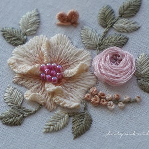 Puede incluir: Dise&ntilde;o floral bordado a mano. Se aprecia una flor grande de color melocot&oacute;n claro con detalles de cuentas rosas, una peque&ntilde;a rosa rosa y hojas verdes. Tambi&eacute;n hay una peque&ntilde;a mariposa melocot&oacute;n y otras flores peque&ntilde;as de color melocot&oacute;n sobre fondo blanco.