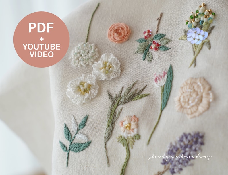 以下が含まれることがあります： クリーム色の生地に、白、ピンク、緑、青で刺繍された様々な花のクローズアップ。画像には、円形のデザインで「PDF + YOUTUBE VIDEO」というテキストが含まれています。刺繍は、詳細なステッチとビーズ細工が特徴です。