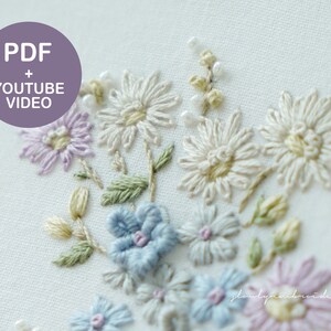May include: Close-up of hand-embroidered flowers in shades of white, lavender, blue, and pink. The floral design includes daisies and other delicate blooms with green leaves. The image includes the text "PDF + YOUTUBE VIDEO" in a purple circle.
