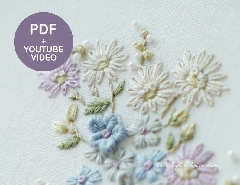May include: Close-up of hand-embroidered flowers in shades of white, lavender, blue, and pink. The floral design includes daisies and other delicate blooms with green leaves. The image includes the text "PDF + YOUTUBE VIDEO" in a purple circle.