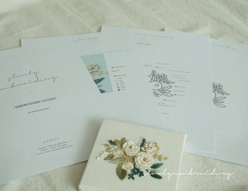 May include: A collection of embroidery guides and a finished embroidery piece. The guides are white with black text and illustrations. The finished piece is a small canvas with a floral design in cream, green, and beige thread. The text "slowly embroidery" is visible.