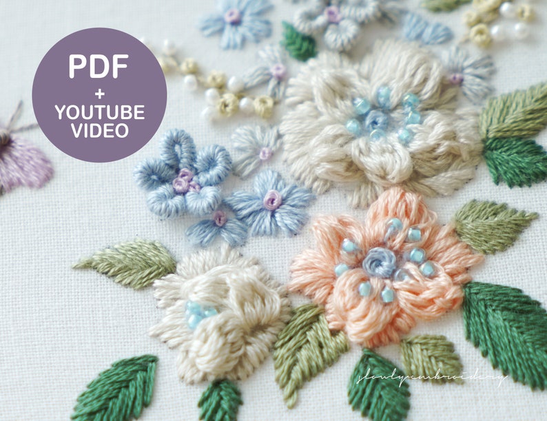 May include: Close-up of a floral embroidery design featuring various flowers in shades of blue, peach, and cream, with green leaves. The embroidery includes bead accents and is set against a white fabric background. Text on the image reads "PDF + YOUTUBE VIDEO".