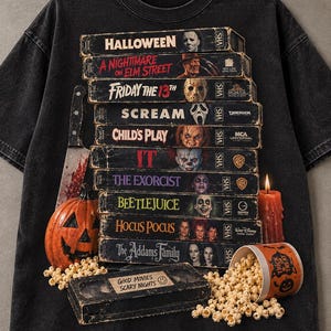 Puede incluir: Una camiseta negra con una pila de cintas VHS de películas de terror que incluyen Halloween, A Nightmare on Elm Street, Friday the 13th, Scream, Child's Play, It, The Exorcist, Beetlejuice, Hocus Pocus y The Addams Family, con calabaza, cuchillo, vela y palomitas.