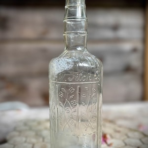 May include: A clear glass bottle with a textured surface and a floral design. The bottle is labeled "W. Stich Co."