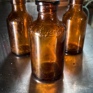 May include: Three amber glass bottles with cork stoppers. The center bottle has the word "Lysol" embossed on the front.