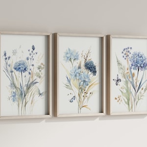May include: A set of three framed watercolor prints featuring blue and green floral bouquets with butterflies. The prints are in simple, light wood frames.