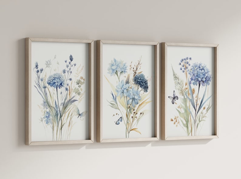 May include: A set of three framed watercolor prints featuring blue and green floral bouquets with butterflies. The prints are in simple, light wood frames.