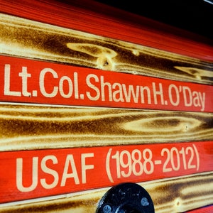 May include: A wooden sign with red, white, and blue stripes. The sign reads "Lt. Col. Shawn H. O'Day USAF (1988-2012)".