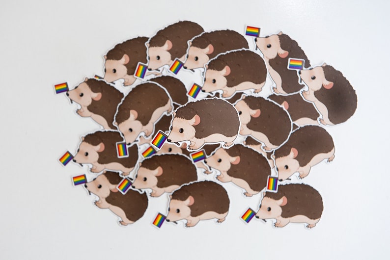 May include: A group of brown hedgehog stickers with rainbow flags. The hedgehogs are arranged in a circle with their heads facing outwards.