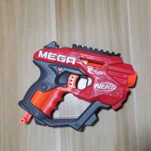 May include: A red and black Nerf Mega Talon blaster with a white "MEGA" and "NERF" logo. The blaster has a black scope and an orange grip.
