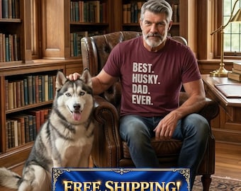 May include: A man in a maroon t-shirt with the text "BEST. HUSKY. DAD. EVER." sits in a leather chair next to a Siberian Husky dog. The room has a library with bookshelves filled with books.