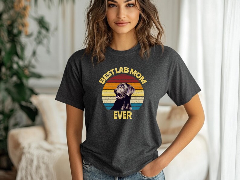 May include: A dark charcoal gray short-sleeve t-shirt featuring a circular graphic with a retro sunset background in orange, yellow, and blue. The graphic displays a black Labrador retriever and the yellow text "BEST LAB MOM EVER".