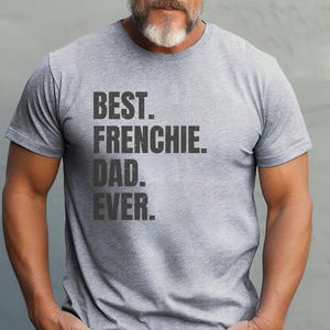 May include: A heather gray t-shirt with the text "BEST. FRENCHIE. DAD. EVER." in a bold, dark gray font. The shirt is short-sleeved and appears to be made of a soft, comfortable material.
