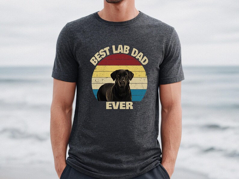 May include: Dark grey t-shirt with a graphic of a black Labrador Retriever and the text "BEST LAB DAD EVER" in a circular design. The design uses a retro colour scheme of red, yellow, and blue.