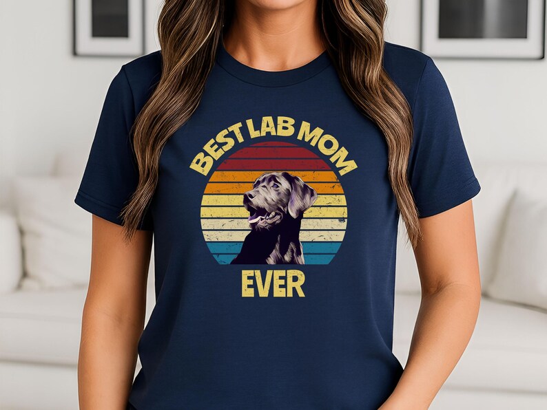 May include: A navy blue short-sleeve t-shirt featuring a graphic of a black Labrador retriever inside a retro-style sunset circle. The text "BEST LAB MOM EVER" is printed in yellow block letters above and below the circular graphic design.