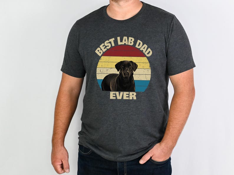 May include: Dark grey t-shirt with a graphic of a black Labrador Retriever inside a retro circle. The circle has a red, yellow, and blue colour scheme, with the text "BEST LAB DAD EVER" in a vintage font.