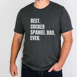 K&ouml;nnte beinhalten: Dunkelgraues T-Shirt mit dem wei&szlig;en Text: "BEST. COCKER SPANIEL DAD. EVER." Das T-Shirt hat einen Rundhalsausschnitt und wird von einer Person getragen. Der Text ist in Gro&szlig;buchstaben.