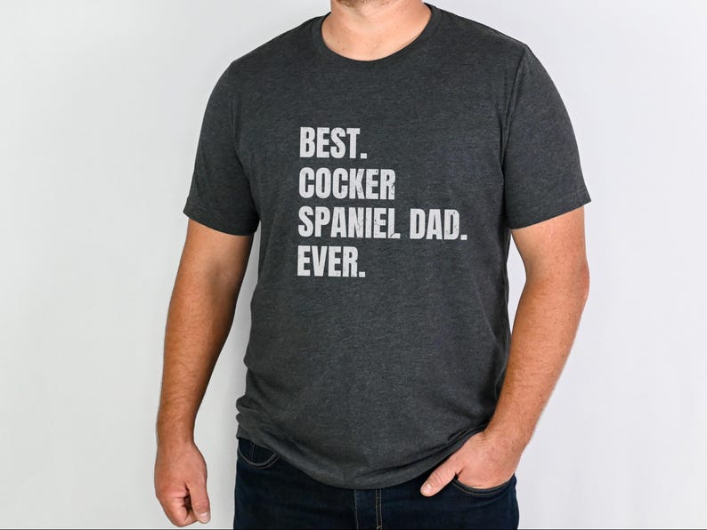 K&ouml;nnte beinhalten: Dunkelgraues T-Shirt mit dem wei&szlig;en Text: "BEST. COCKER SPANIEL DAD. EVER." Das T-Shirt hat einen Rundhalsausschnitt und wird von einer Person getragen. Der Text ist in Gro&szlig;buchstaben.