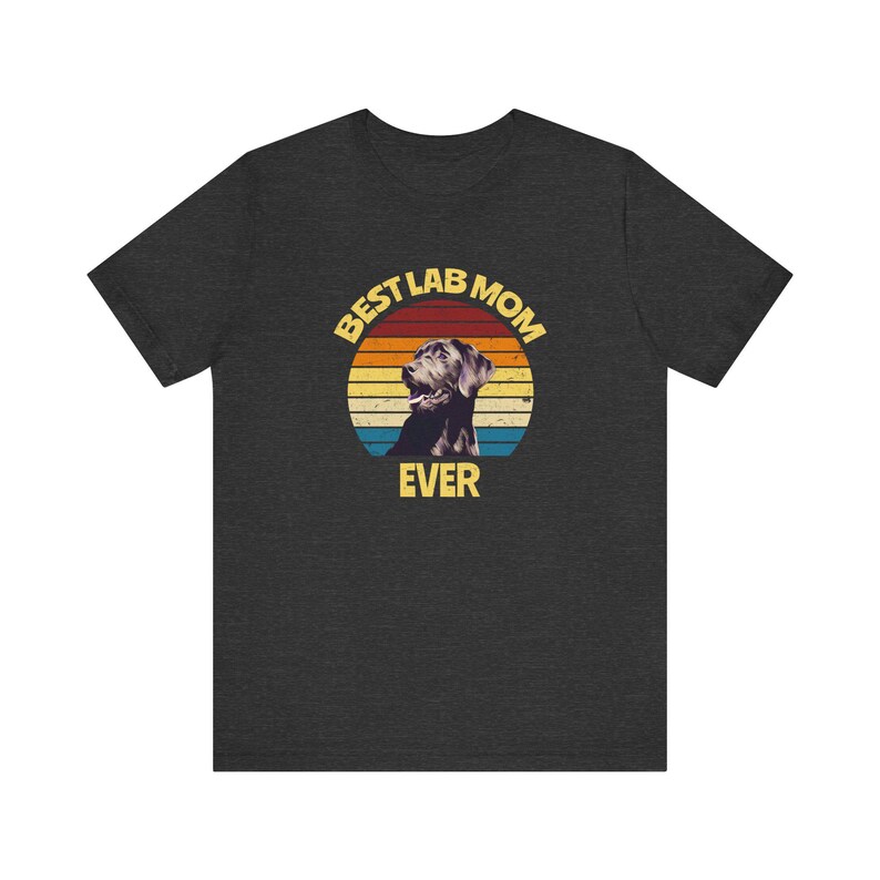 May include: A dark heather gray short-sleeve t-shirt featuring a circular graphic with a sunset background of orange, yellow, and blue stripes. The graphic includes a black Labrador dog illustration and the yellow text BEST LAB MOM EVER.