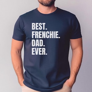 May include: Navy blue t-shirt with the text "BEST. FRENCHIE. DAD. EVER." in white block letters. The shirt is a crew neck and appears to be made of a soft material. The shirt is being worn by a person.