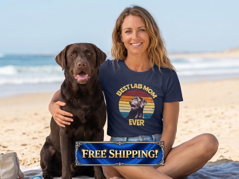 May include: A navy blue short-sleeved t-shirt featuring a circular graphic with a retro sunset design in orange, yellow, and teal. The graphic includes a silhouette of a Labrador retriever and the text BEST LAB MOM EVER in a bold yellow font.