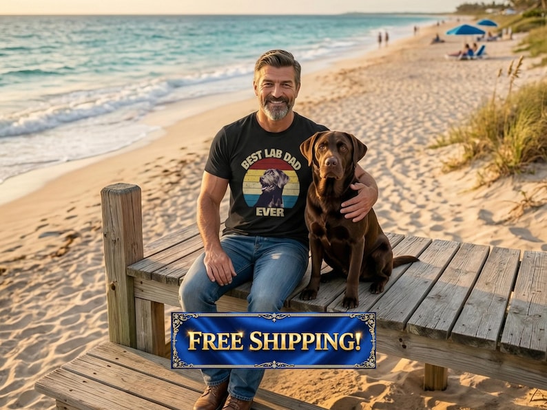 以下が含まれることがあります： 「Best Lab Dad Ever」と書かれたレトロなデザインの黒いTシャツを着た男性が、茶色のラブラドールレトリバーと一緒に木のドックに座っています。背景にはビーチと海が写っています。