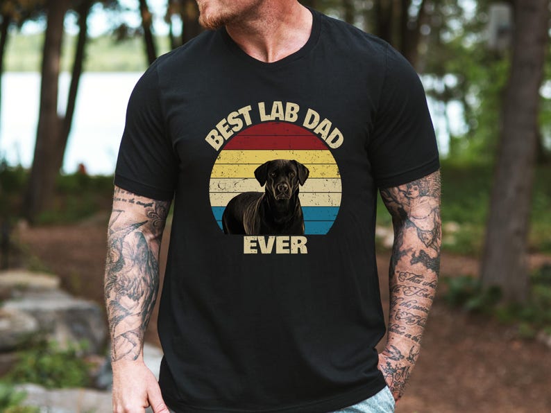 May include: Black t-shirt with a graphic of a black Labrador Retriever in a circular design with red, yellow, and blue stripes. The text "BEST LAB DAD EVER" is arched above and below the dog image.