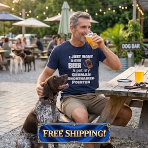 May include: A man drinking beer while petting a German Shorthaired Pointer dog. He is wearing a navy blue t-shirt with the text "I just want to drink beer & pet my German Shorthaired Pointer." The dog is brown and white.