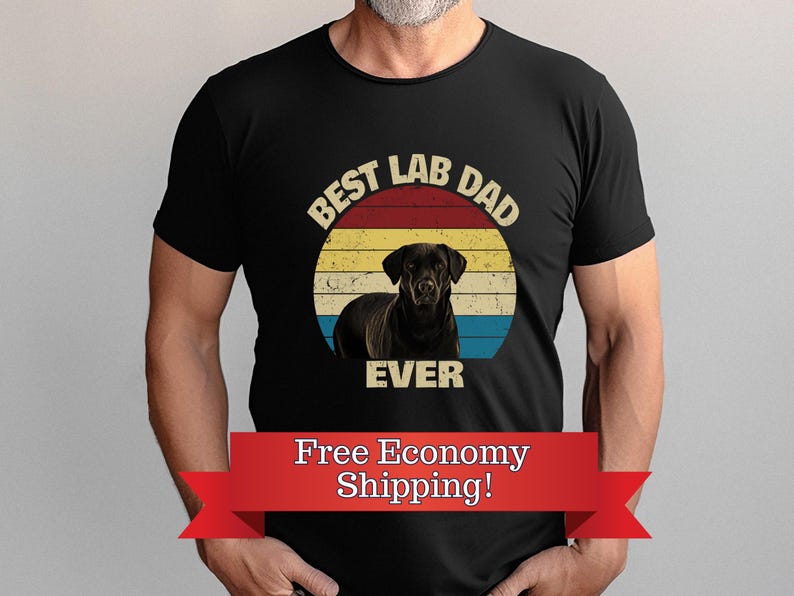 May include: Black t-shirt with a graphic of a black Labrador Retriever inside a circular design with a red, yellow, and blue striped background. The text "BEST LAB DAD EVER" is printed above and below the dog image.