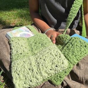 May include: A green crocheted tote bag with a book titled "The Joy of" inside. The bag has a long green strap and is made with a gradient of green yarn.