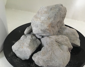 May include: A close-up of a pile of grey clay rocks on a black plate. The rocks are rough and have a natural texture.