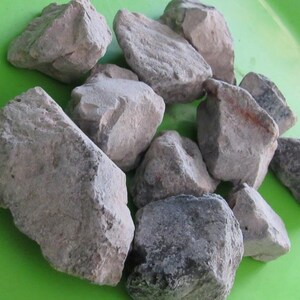 May include: A collection of grey and white rocks on a green surface. The rocks are various sizes and shapes.