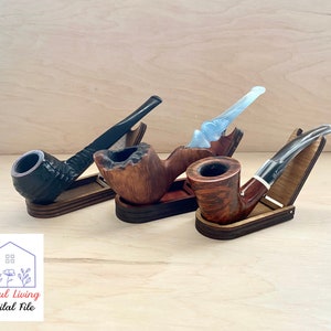 May include: Three wooden pipe stands with three different pipes. The stands are made of wood and have a natural finish. The pipes are made of different materials, including wood, metal, and acrylic. The pipes are all in different styles and sizes.