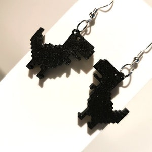 May include: A pair of black pixelated dinosaur earrings with silver hooks.