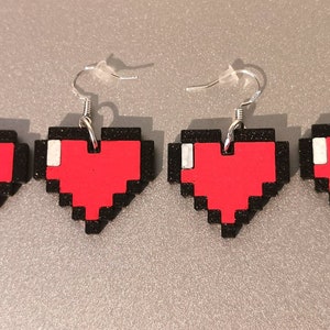 May include: Four pairs of pixel heart earrings. Each earring features a red pixelated heart with a black outline and a silver hook.