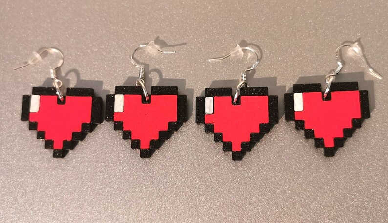 May include: Four pairs of pixel heart earrings. Each earring features a red pixelated heart with a black outline and a silver hook.