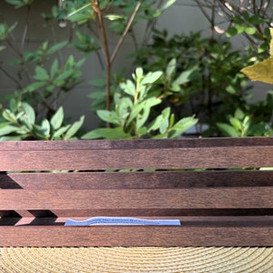 May include: A dark brown wooden crate with three horizontal slats. The crate is sitting on a woven placemat.