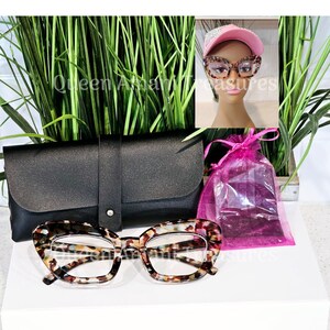May include: A pair of tortoise shell cat eye reading glasses with a black case and a pink drawstring bag. The glasses have a clear lens.