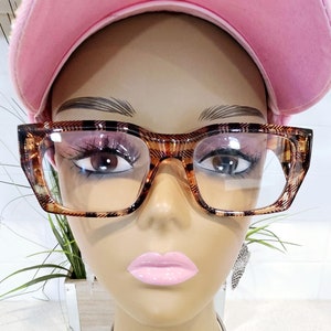 May include: A mannequin wearing a pink baseball cap, tortoiseshell glasses, and a silver necklace with a pendant shaped like the continent of Africa.