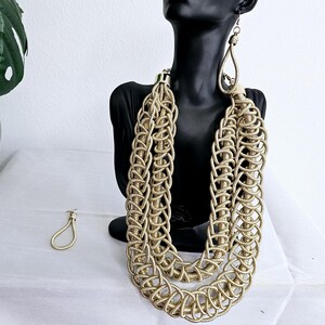 May include: A gold-toned multi-strand necklace with a woven chain design. The necklace is layered and has a chunky, statement look.