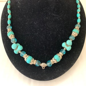 May include: A turquoise and silver beaded necklace with a clasp closure. The necklace features turquoise beads of varying sizes and shapes, as well as silver beads with decorative details.