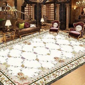 May include: A white area rug with a floral pattern and a decorative border. The rug is in a large room with a couch and chairs.