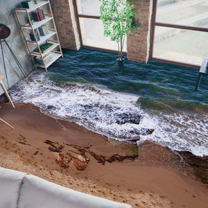 Puede incluir: Un revestimiento de suelo realista en forma de ola de océano con una costa de playa de arena. El revestimiento de suelo está instalado en una habitación con una estantería, un escritorio y una planta.