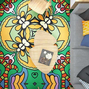 May include: A green, yellow, blue, orange, and red patterned rug with a wooden chair and two wooden triangular tables. One table has a small white tray with a white flower on it.