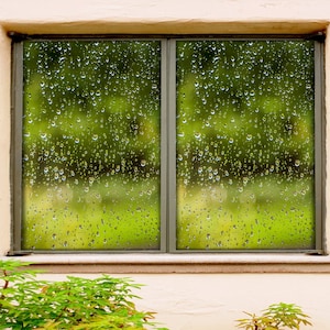 Puede incluir: Una ventana con vista a un paisaje verde y frondoso. La ventana está cubierta de gotas de lluvia, creando un efecto borroso. El marco de la ventana es gris y la pared es blanca.